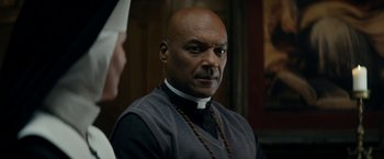 Movie still from “Prey for the Devil” (2022), directed by Daniel Stamm – A bald man wearing a priest's collar; Close Up shot, Low angle