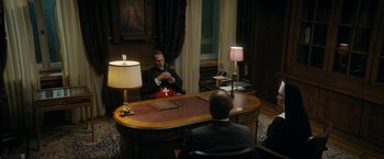 Movie still from “Prey for the Devil” (2022), directed by Daniel Stamm – A man sitting in front of a mirror in front of a desk; Wide shot, High angle