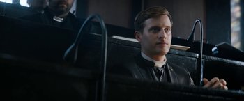 Movie still from “Prey for the Devil” (2022), directed by Daniel Stamm – A man in a suit and tie sitting in a chair; Close Up shot, Low angle