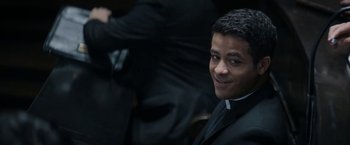 Movie still from “Prey for the Devil” (2022), directed by Daniel Stamm – A man in a priest's outfit smiling for the camera; Close Up shot, Over the shoulder angle