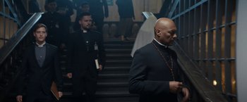 Movie still from “Prey for the Devil” (2022), directed by Daniel Stamm – Two men in black suits are walking down the stairs; Medium shot, Low angle