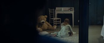 Movie still from “Prey for the Devil” (2022), directed by Daniel Stamm – A little girl sitting on the floor next to a large teddy bear; Wide shot, High angle