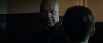 Movie still from “Prey for the Devil” (2022), directed by Daniel Stamm – A bald man wearing a priest's outfit and wearing a rosary; Close Up shot, Over the shoulder angle