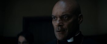 Movie still from “Prey for the Devil” (2022), directed by Daniel Stamm – A man with a bald head wearing a priest's outfit; Close Up shot, Low angle
