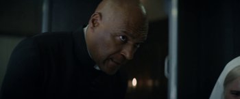 Movie still from “Prey for the Devil” (2022), directed by Daniel Stamm – A bald man in a black shirt and a white shirt; Close Up shot, Low angle