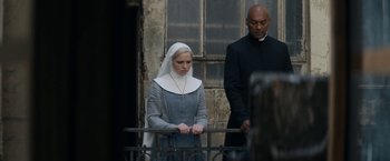 Movie still from “Prey for the Devil” (2022), directed by Daniel Stamm – A nun and a priest standing in front of a building; Medium shot, Low angle