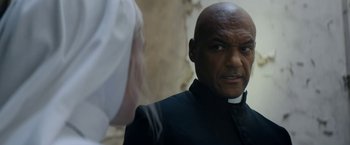 Movie still from “Prey for the Devil” (2022), directed by Daniel Stamm – A man wearing a priest's outfit looking at another man; Close Up shot, Low angle