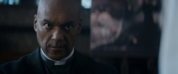 Movie still from “Prey for the Devil” (2022), directed by Daniel Stamm – A man in a black suit and white shirt looking at the camera; Close Up shot, Low angle