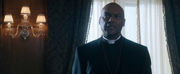 Movie still from “Prey for the Devil” (2022), directed by Daniel Stamm – A man in a priest's outfit looking at the camera; Close Up shot, Low angle