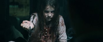 Movie still from “Prey for the Devil” (2022), directed by Daniel Stamm – A young girl with blood on her face holding a knife; Close Up shot, High angle