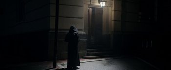 Movie still from “Prey for the Devil” (2022), directed by Daniel Stamm – A person dressed as a monk standing in front of a building; Wide shot, Low angle
