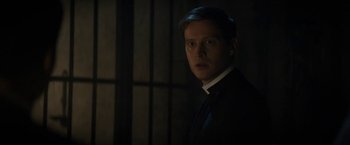 Movie still from “Prey for the Devil” (2022), directed by Daniel Stamm – A man in a suit standing in a dark room; Close Up shot, Over the shoulder angle