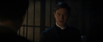 Movie still from “Prey for the Devil” (2022), directed by Daniel Stamm – A man wearing a priest's outfit in a dark room; Close Up shot, Over the shoulder angle