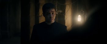 Movie still from “Prey for the Devil” (2022), directed by Daniel Stamm – A young man in a priest's outfit looking at the camera; Medium shot, Low angle