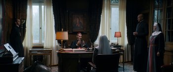 Movie still from “Prey for the Devil” (2022), directed by Daniel Stamm – A man sitting at a desk in front of a woman; Wide shot, High angle