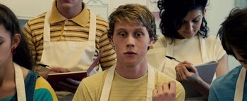 Movie still from “Pride” (2014), directed by Matthew Warchus – A young man wearing an apron in front of a group of people; Close Up shot, Over the shoulder angle