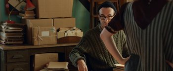 Movie still from “Pride” (2014), directed by Matthew Warchus – A man sitting at a table with a stack of books; Medium shot, Over the shoulder angle