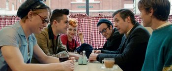 Movie still from “Pride” (2014), directed by Matthew Warchus – A group of people sitting at a table with drinks; Medium shot, Over the shoulder angle