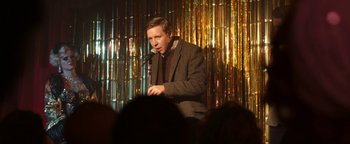 Movie still from “Pride” (2014), directed by Matthew Warchus – A man standing in front of a microphone on a stage; Medium shot, Over the shoulder angle