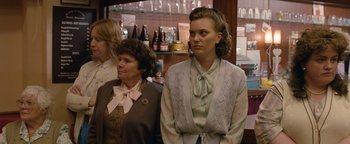 Movie still from “Pride” (2014), directed by Matthew Warchus – Two women standing next to each other in front of bottles; Medium shot, Over the shoulder angle