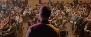 Movie still from “Pride” (2014), directed by Matthew Warchus – A man standing in front of a crowd of people; Wide shot, Over the shoulder angle