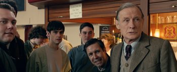 Movie still from “Pride” (2014), directed by Matthew Warchus – A group of men standing next to each other in a room; Medium shot, Over the shoulder angle