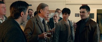Movie still from “Pride” (2014), directed by Matthew Warchus – A group of men standing around each other holding drinks; Medium shot, Over the shoulder angle