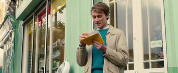 Movie still from “Pride” (2014), directed by Matthew Warchus – A young man reading a book outside a store; Medium shot, Over the shoulder angle