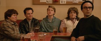 Movie still from “Pride” (2014), directed by Matthew Warchus – A group of people sitting at a table with drinks; Medium shot, Over the shoulder angle