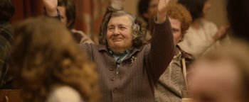 Movie still from “Pride” (2014), directed by Matthew Warchus – An older woman raises her hand in a crowd; Medium shot, Low angle