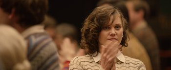 Movie still from “Pride” (2014), directed by Matthew Warchus – A woman with brown curly hair and a white shirt is holding her hand up to her face; Close Up shot, Over the shoulder angle