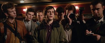 Movie still from “Pride” (2014), directed by Matthew Warchus – A group of young men standing next to each other in a room; Medium shot, Over the shoulder angle