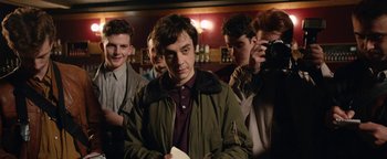 Movie still from “Pride” (2014), directed by Matthew Warchus – A group of men standing around a bar; Medium shot, Over the shoulder angle