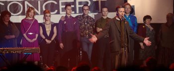 Movie still from “Pride” (2014), directed by Matthew Warchus – A group of men standing on a stage with a microphone; Medium shot, Over the shoulder angle