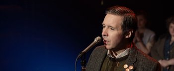 Movie still from “Pride” (2014), directed by Matthew Warchus – A man is speaking into a microphone on a stage; Close Up shot, Over the shoulder angle