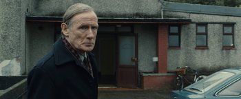 Movie still from “Pride” (2014), directed by Matthew Warchus – An older man standing in front of a brick building; Medium shot, Over the shoulder angle