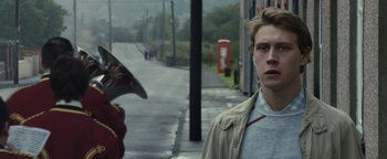 Movie still from “Pride” (2014), directed by Matthew Warchus – A man standing next to another man on the sidewalk; Close Up shot, Over the shoulder angle