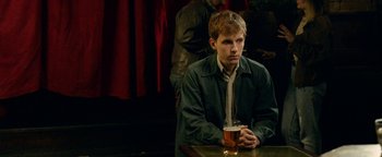 Movie still from “Pride” (2014), directed by Matthew Warchus – A man sitting at a table with a glass of beer in front of him; Medium shot, Over the shoulder angle