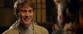 Movie still from “Pride” (2014), directed by Matthew Warchus – A young man smiling for the camera in front of a group of people; Close Up shot, Over the shoulder angle