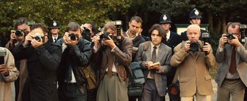 Movie still from “Pride” (2014), directed by Matthew Warchus – A group of people standing around taking pictures of each other; Medium shot, Over the shoulder angle