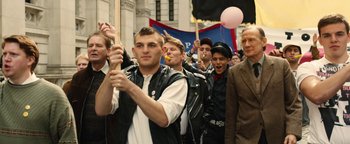 Movie still from “Pride” (2014), directed by Matthew Warchus – A group of people marching down a street; Medium shot, Over the shoulder angle