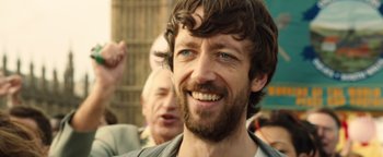 Movie still from “Pride” (2014), directed by Matthew Warchus – A person with a beard smiling; Close Up shot, Over the shoulder angle
