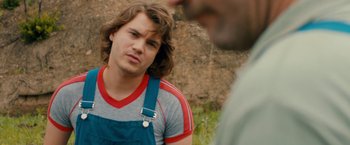 Movie still from “Prince Avalanche” (2013), directed by David Gordon Green – A man with long brown hair wearing a red and blue striped shirt; Close Up shot, Over the shoulder angle