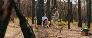 Movie still from “Prince Avalanche” (2013), directed by David Gordon Green – A man sitting in a chair next to another man in the woods; Wide shot, High angle