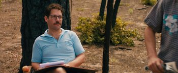 Movie still from “Prince Avalanche” (2013), directed by David Gordon Green – A man sitting on the ground reading a book; Medium shot, Over the shoulder angle