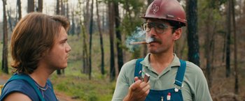 Movie still from “Prince Avalanche” (2013), directed by David Gordon Green – A man in a hard hat smoking a cigar in the woods; Medium shot, Low angle