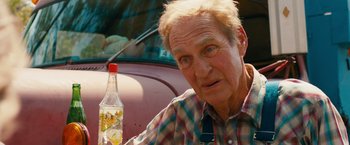 Movie still from “Prince Avalanche” (2013), directed by David Gordon Green – An older man sitting at a table with a bottle of water; Close Up shot, Over the shoulder angle