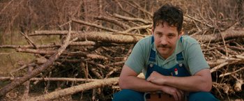 Movie still from “Prince Avalanche” (2013), directed by David Gordon Green – A man sitting on the ground in front of a pile of wood; Close Up shot, Over the shoulder angle