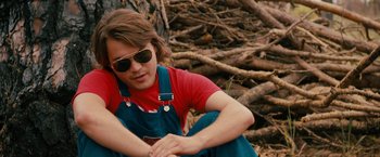 Movie still from “Prince Avalanche” (2013), directed by David Gordon Green – A woman sitting on the ground near a pile of tree branches; Medium shot, Low angle