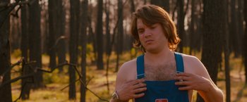 Movie still from “Prince Avalanche” (2013), directed by David Gordon Green – A man with a beard and a blue apron is standing in the woods; Medium shot, Over the shoulder angle